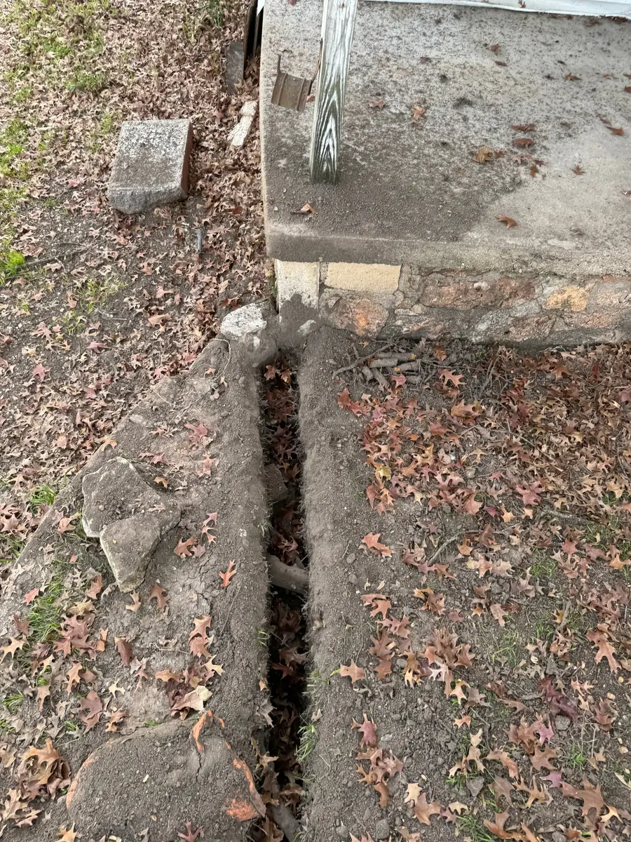 Narrow air spade trench opened along a building slab with a tree root left intact, spanning the open trench
