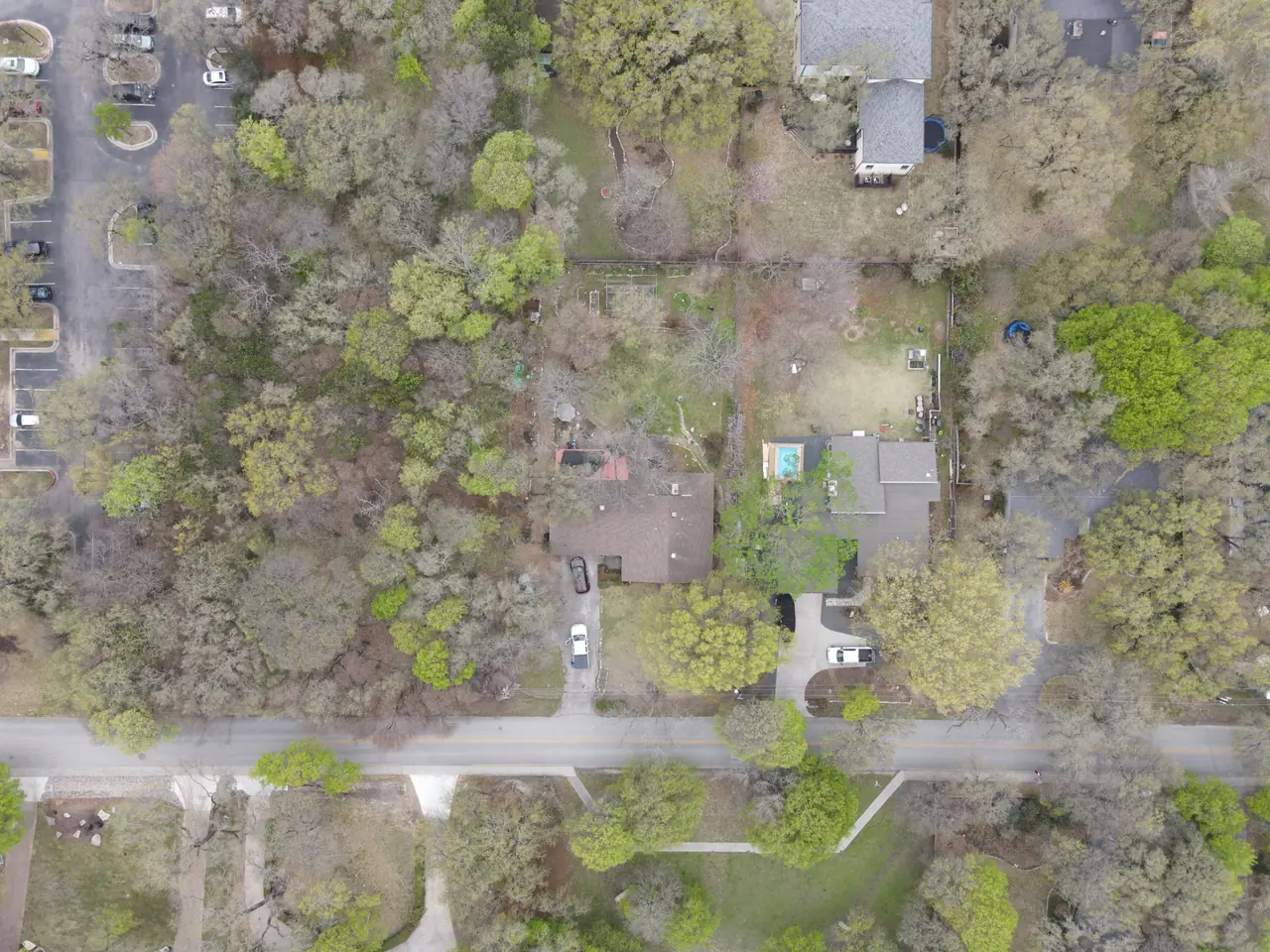 Aerial view looking down on a wooded property, a house and drive threaded between mature tree canopies