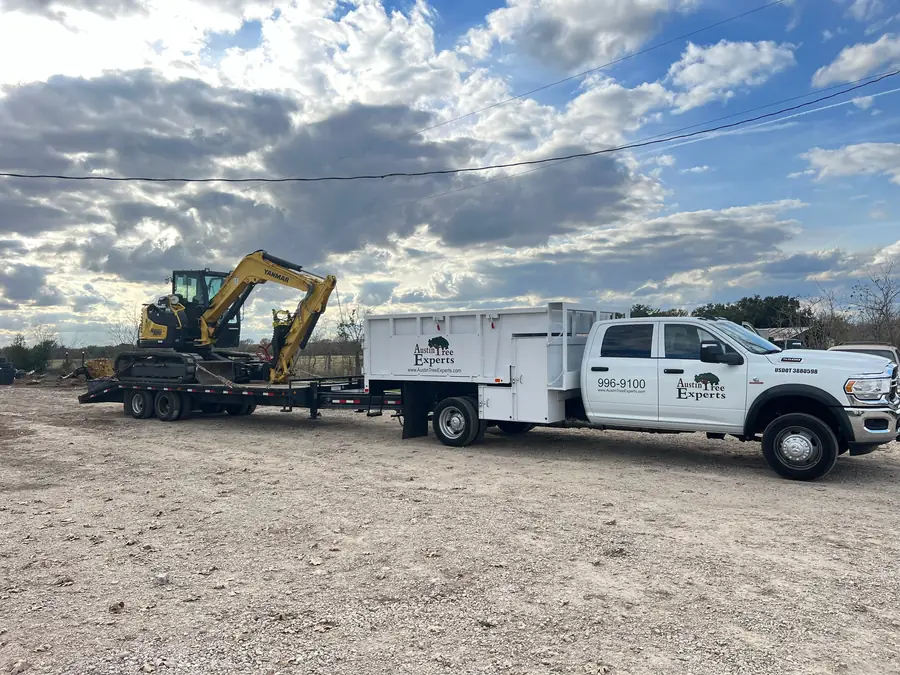 Yanmar mini excavator fitted with a log and brush grapple, chained to a pintle-hitch trailer behind an Austin Tree Experts crew truck