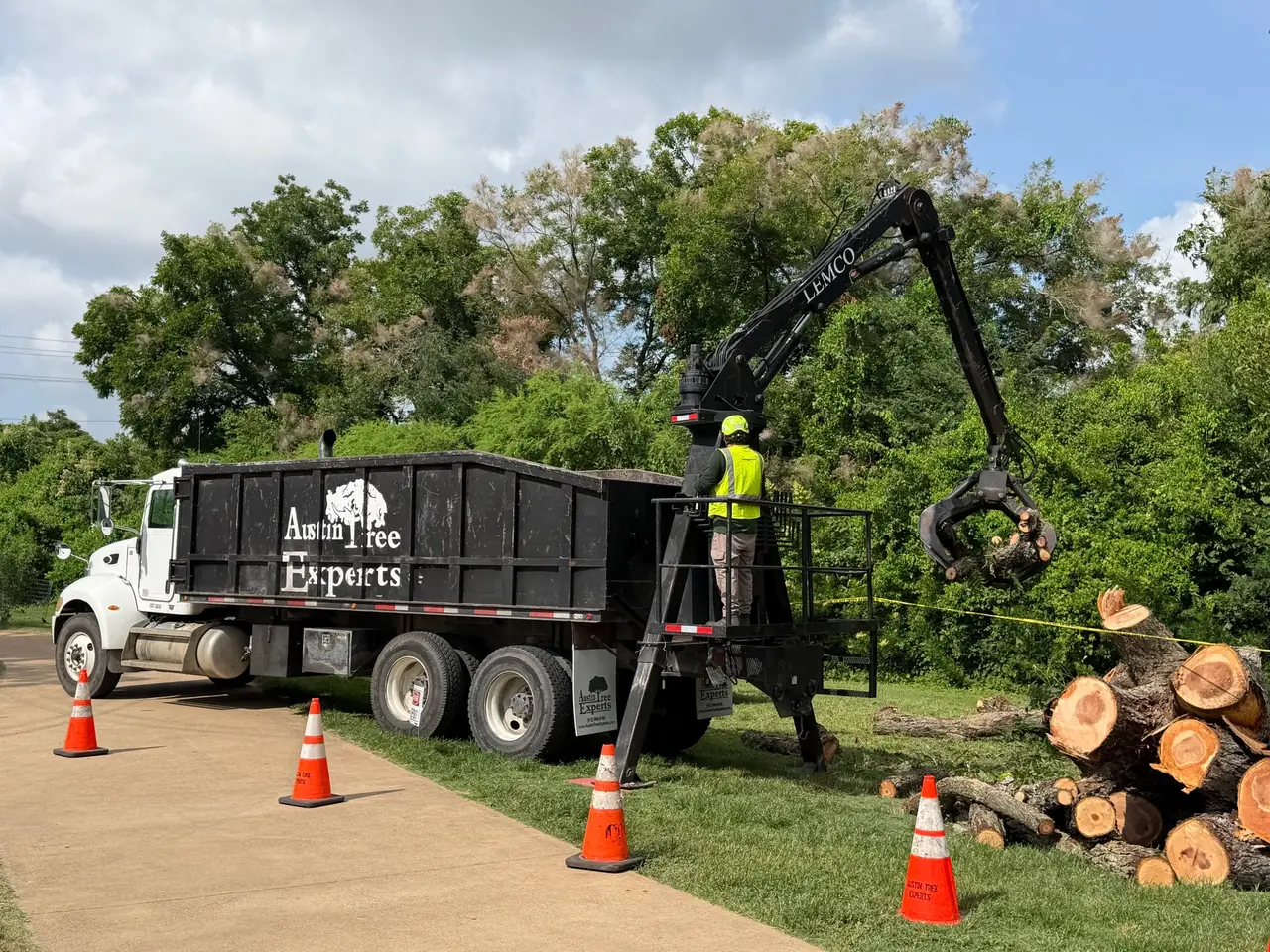 Knuckleboom grapple loader lifting cut log rounds into an Austin Tree Experts dump body, the operator working the controls from the deck platform