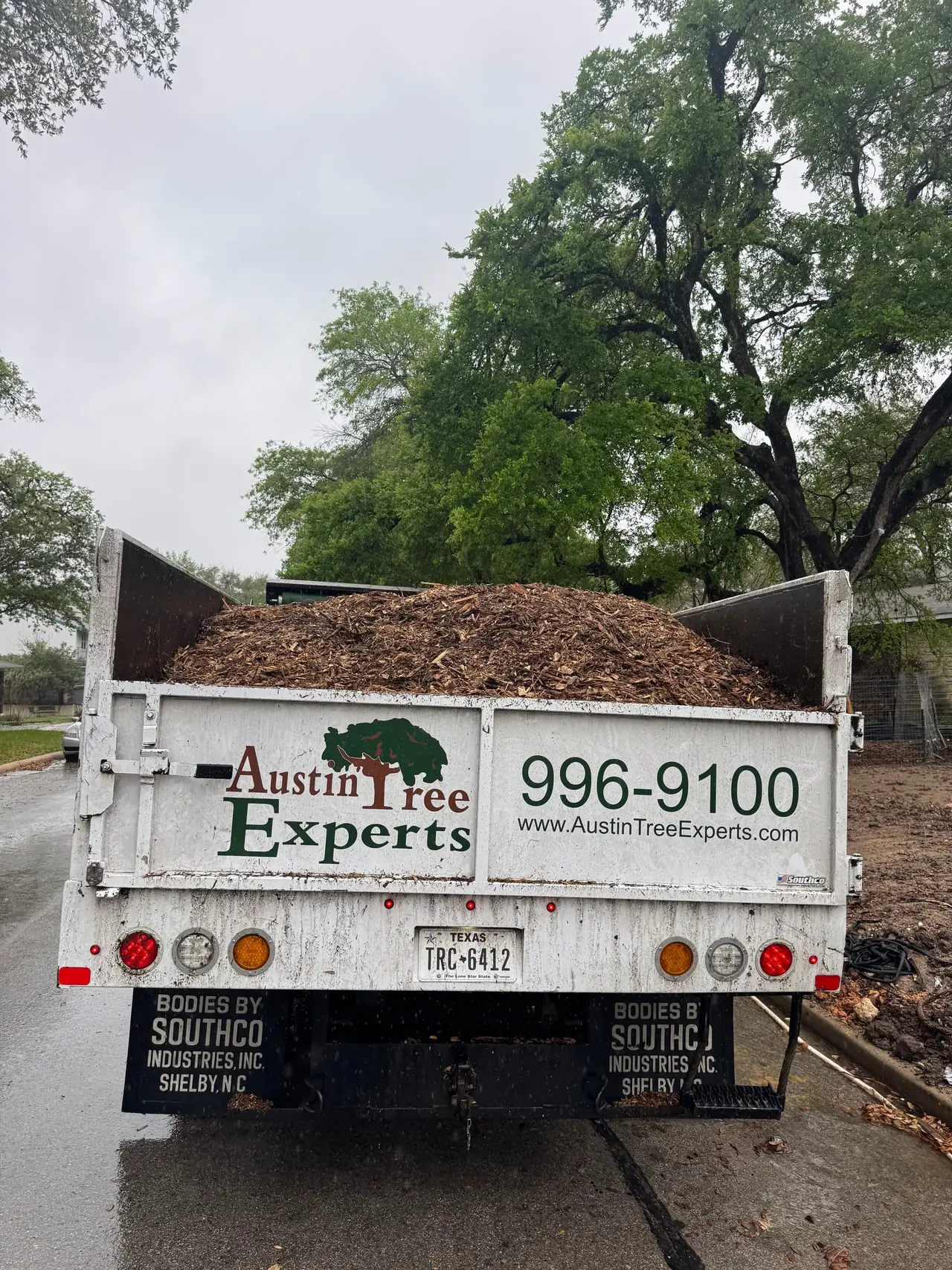 Austin Tree Experts dump truck loaded with wood-chip mulch for delivery, the company name, phone number and web address lettered across the tailgate