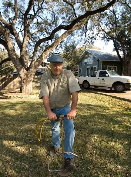 Arborist operating a soil injection probe in a lawn beneath mature live oaks, beside a branded Austin Tree Experts truck