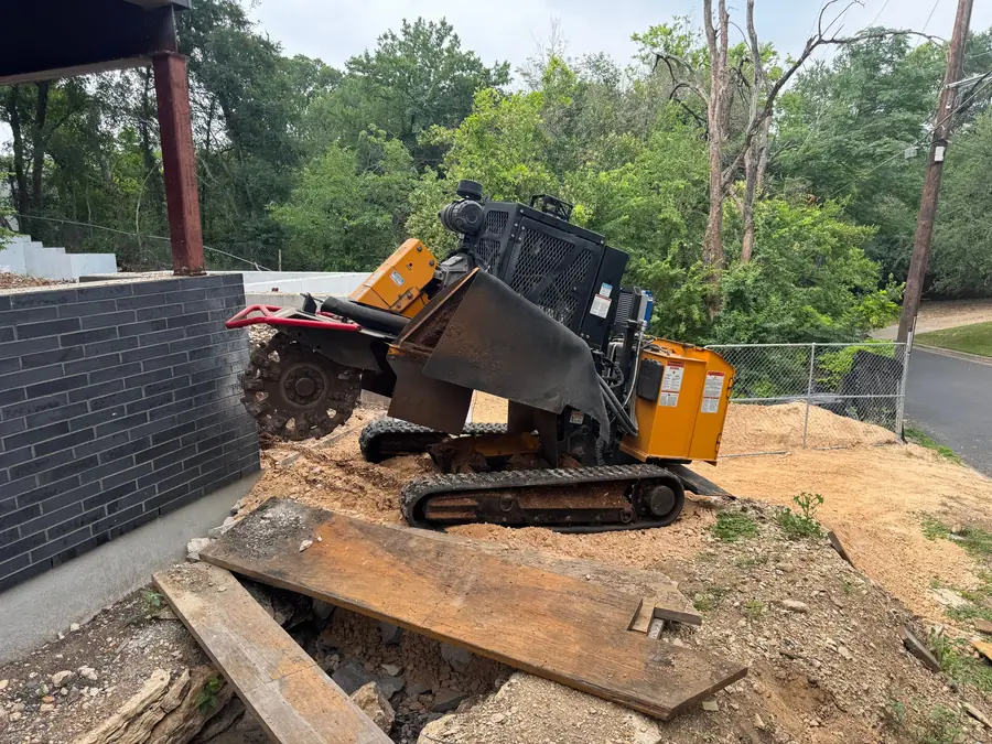 Tracked stump grinder working a stump beside a masonry wall
