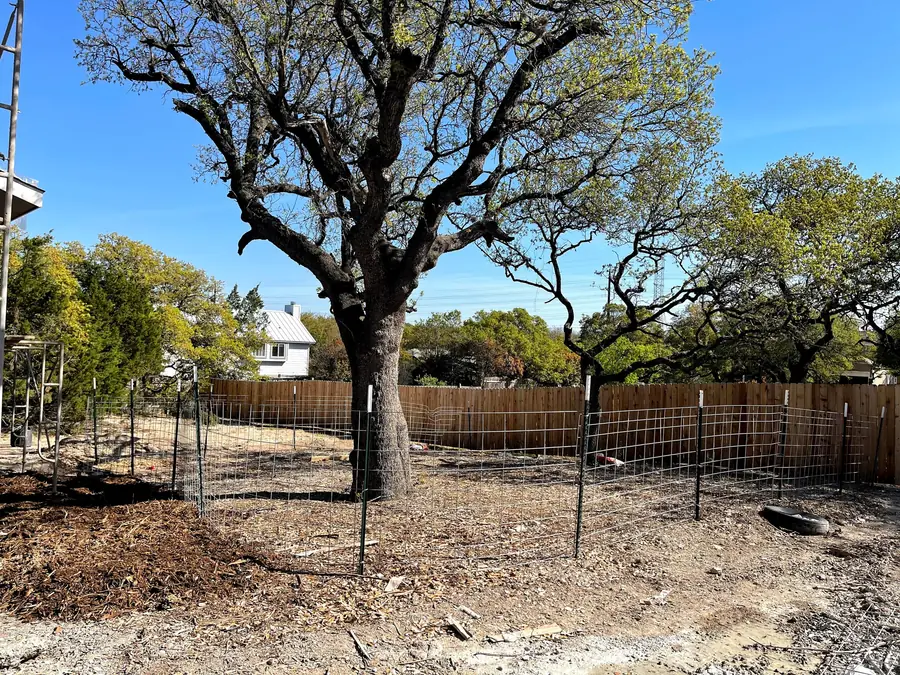 Welded wire fencing on steel posts enclosing a wide mulched area around a mature live oak on a cleared construction site