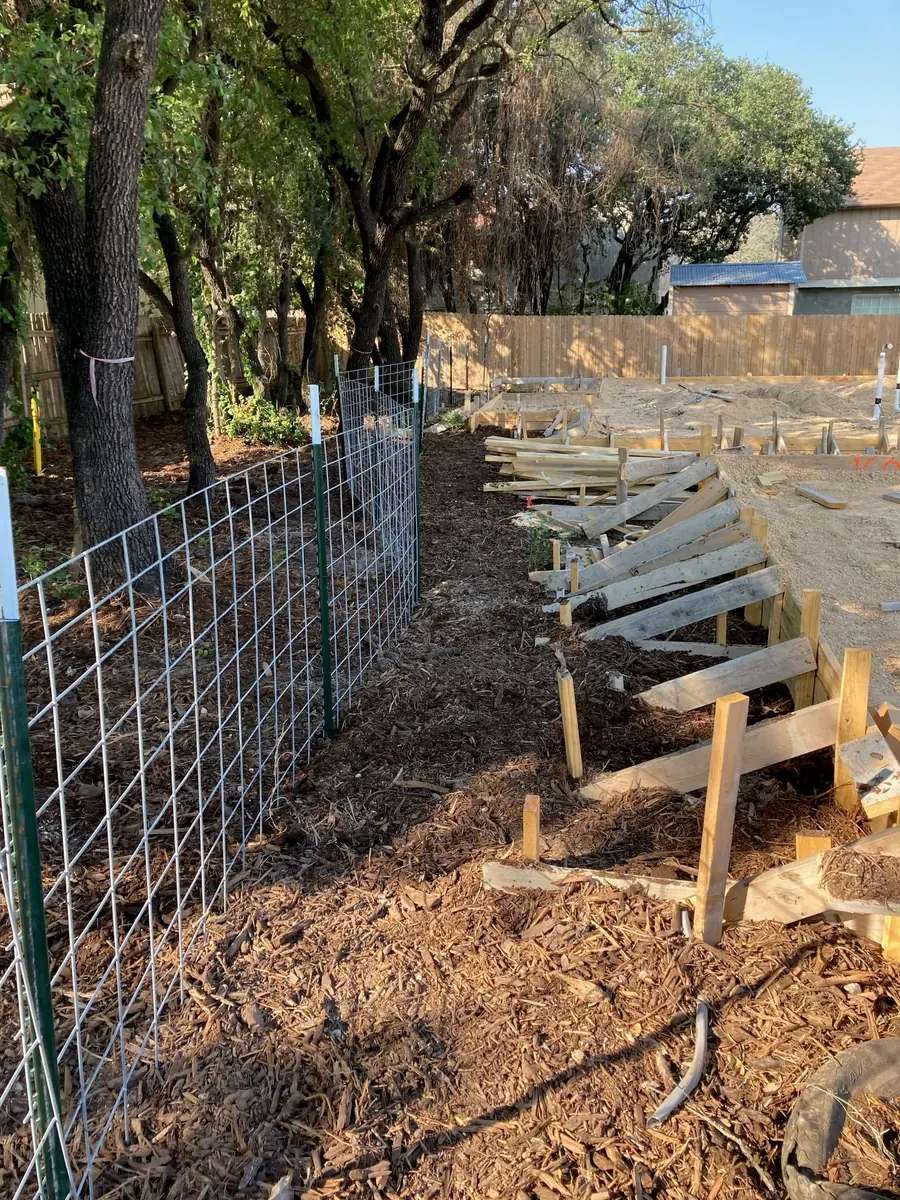 Welded wire tree protection fence on steel posts enclosing a mulched critical root zone, with foundation forms under construction beyond it